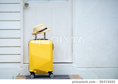 Yellow suitcase, luggage with hat at front door, Leaving home for a holiday and vacation, travel, get ready for adventure. 96459888