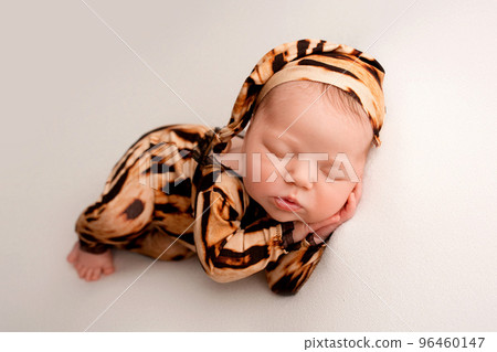 Sleeping newborn girl in the first days of life on a white background. Macro studio portrait of a child. Image of a tiger cub. Newborn baby in tiger pajamas. Striped black and orange baby clothes. Sleeping newborn girl in the first days of life on a white background. Macro studio portrait of a child. Image of a tiger cub. Newborn baby in tiger pajamas. Striped black and orange baby clothes. 96460147