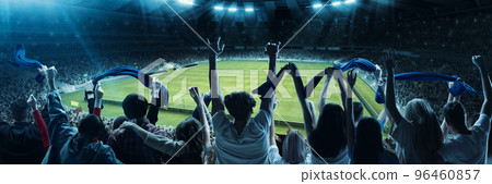 Back view of excited football soccer fans cheering their team with blue scarfs at crowded stadium at evening time. Concept of sport, cup, world, team, event, competition 96460857