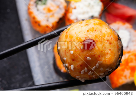 baked sushi roll holding by sticks. sushi rolls served at grey tray. flat lay. close up baked sushi roll holding by sticks. sushi rolls served at grey tray. flat lay. close up 96460948