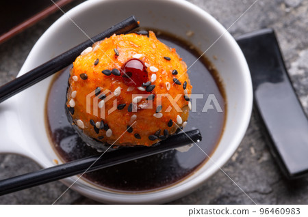 baked sushi roll holding by sticks under soy souce. sushi rolls served at grey  tray. flat lay. close up 96460983