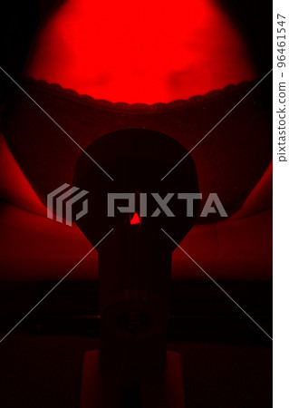 Woman sitting on chair with a heat lamp on her lower back Woman sitting on chair with a heat lamp on her lower back 96461547