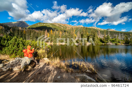 Hiker near mountain lake called Jamske pleso in autumn colors with peak Krivan at background. Slovakia 96461724