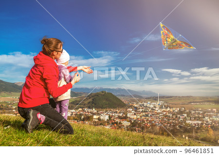 Mother and daughter playfull with kite in field over town Mother and daughter playfull with kite in field over town 96461851
