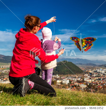 Mother and little daughter play with kite at the sunny field over city Mother and little daughter play with kite at the sunny field over city 96461852