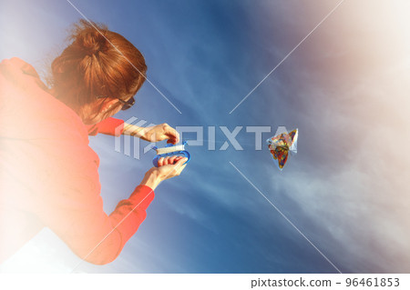 Young woman with flying colorful kite over clear blue sky Young woman with flying colorful kite over clear blue sky 96461853