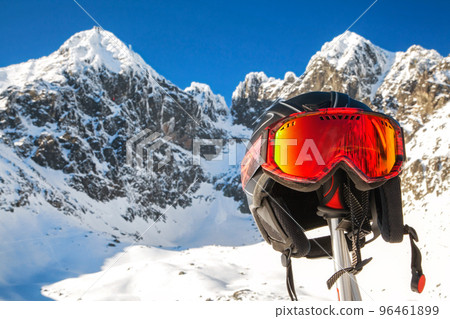 Ski helmet and googles on ski pole with snowy peaks at background 96461899