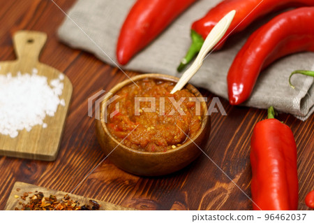 Ajvar from paprika, tomatoes, garlic and onions with spices on a brown wooden table. Balkan food. Selective focus Ajvar from paprika, tomatoes, garlic and onions with spices on a brown wooden table. Balkan food. Selective focus 96462037