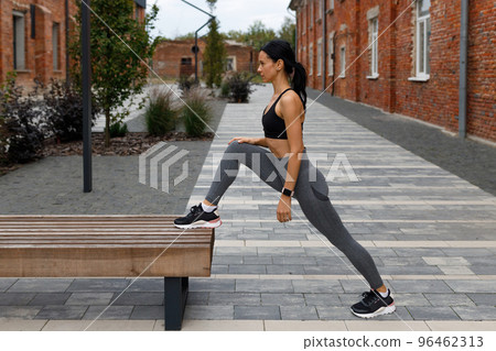 Side view of fitness woman stretching leg on street bench 96462313