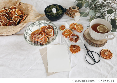 Traditional Christmas still life. Cup of tea, dry oranges and pine, eucalyptus tree branches on white linen table cloth. Blank greeting card mockup. Festive craft table setting. Selective focus. 96463044
