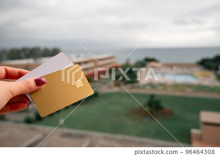 Golden and White Bank Card In Woman Hand On Background Of Hotel Bungalow And Pool In Moraitika, Corfu, Greece. The Concept Of Payment For Relax And Unlimited Possibilities. Golden and White Bank Card In Woman Hand On Background Of Hotel Bungalow And Pool In Moraitika, Corfu, Greece. The Concept Of Payment For Relax And Unlimited Possibilities. 96464308