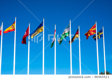 Flags of Different Countries Hang On Flagpoles Against Blue Sky. Flag of Spain, Ukraine, Germany, Sweden, Turkey, Uzbekistan and Macedonia. The concept of support and unity of countries. 96464421