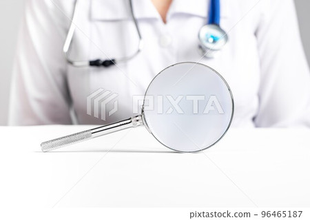 Doctor sitting at table with magnifier. Medical checkup, diseases prevention and diagnosis concept. Woman with stethoscope in lab coat Doctor sitting at table with magnifier. Medical checkup, diseases prevention and diagnosis concept. Woman with stethoscope in lab coat 96465187