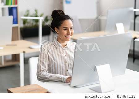 Happy latin businesswoman working with modern computer, checking email, sitting at her workplace in office interior 96467122