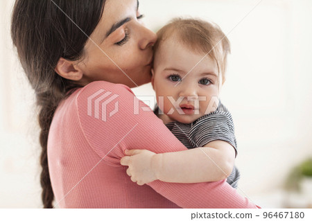 Caring young mother holding and kissing sweet... - Stock Photo