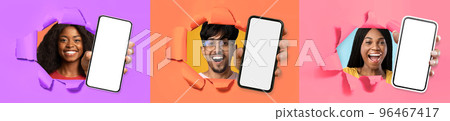 Three cheerful youngsters showing smartphones through hole in paper wall 96467417