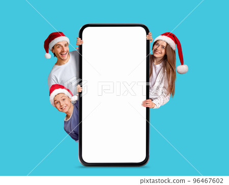 Happy caucasian little boy and millennial couple in Santa Claus hats with big smartphone with empty screen 96467602
