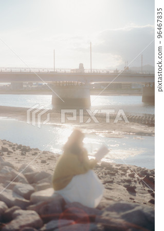 Photo of a young woman standing while reading a book on the riverbed 96467835