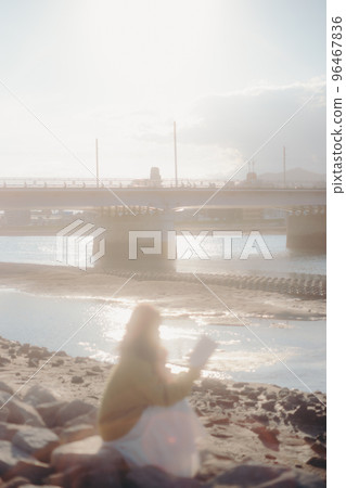 Photo of a young woman standing while reading a book on the riverbed Photo of a young woman standing while reading a book on the riverbed 96467836