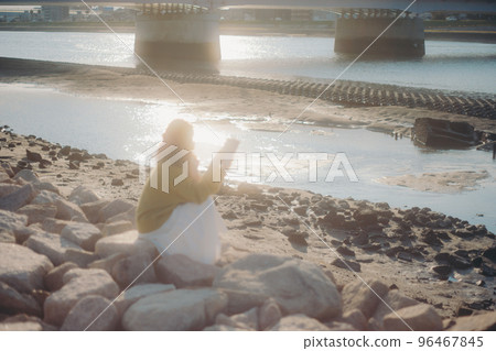 Photo of a young woman standing while reading a book on the riverbed 96467845