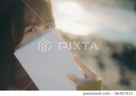 Photo of a young woman standing while reading a book on the riverbed Photo of a young woman standing while reading a book on the riverbed 96467913