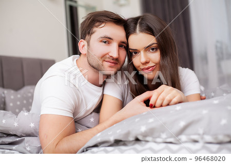 Happy sensual young couple lying in bed together Happy sensual young couple lying in bed together 96468020