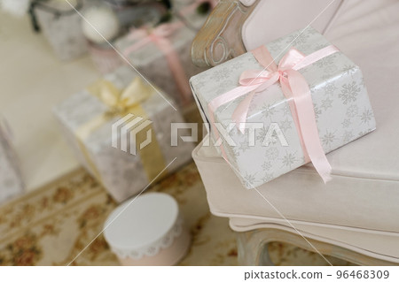 Beautiful Christmas present with silver snowlakes and pink ribbon lying on a chair near christmas tree 96468309