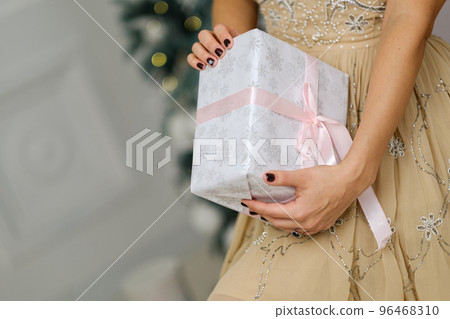 Closeup shot of female hands holding beautiful Christmas present with pink ribbon on white background in interior 96468310