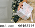 Closeup shot of female hands holding beautiful Christmas present with pink ribbon on white background in interior 96468346