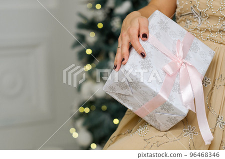 Closeup shot of female hands holding beautiful Christmas present with pink ribbon on white background in interior 96468346