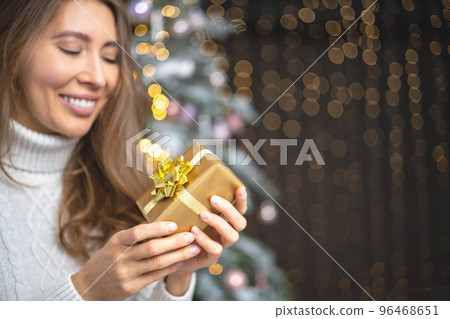 Closeup smiling young blonde woman holding luxury golden Christmas gift box celebrating holiday 96468651