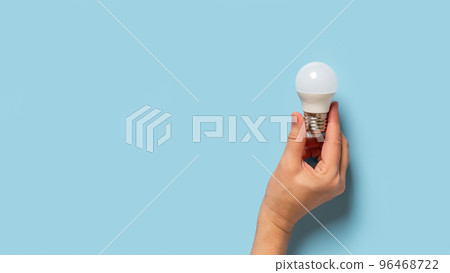 Light bulb in female fingers over blue background. Light bulb in female fingers over blue background. 96468722
