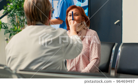 Physician doing consultation with asian woman in hospital lobby, wearing cervical collar. Patient with foam brace doing eyesight exam to check brain damage with after injury. Handheld shot. Physician doing consultation with asian woman in hospital lobby, wearing cervical collar. Patient with foam brace doing eyesight exam to check brain damage with after injury. Handheld shot. 96469497
