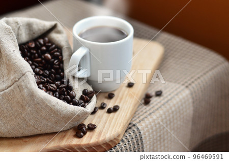A full bag of brown coffee beans and a white cup of hot coffee l 96469591