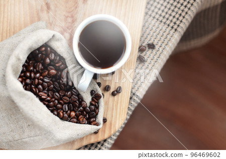 A full bag of brown coffee beans and a white cup of hot coffee l A full bag of brown coffee beans and a white cup of hot coffee l 96469602