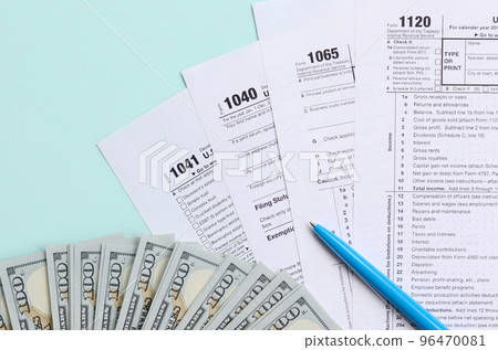 Tax forms lies near hundred dollar bills and blue pen on a light blue background. Income tax return Tax forms lies near hundred dollar bills and blue pen on a light blue background. Income tax return 96470081