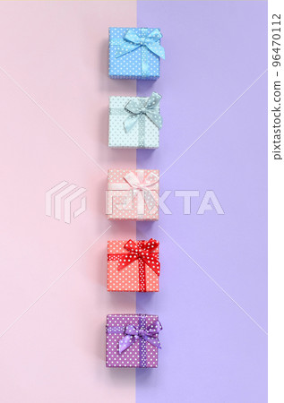 Small gift boxes of different colors with ribbons lies on a violet and pink color background Small gift boxes of different colors with ribbons lies on a violet and pink color background 96470112