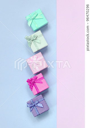 Small gift boxes of different colors with ribbons lies on a violet and pink background Small gift boxes of different colors with ribbons lies on a violet and pink background 96470296