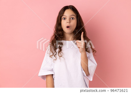 Portrait of surprised little girl wearing white T-shirt raising finger up, has sudden great idea, looking at camera with open mouth. Indoor studio shot isolated on pink background. Portrait of surprised little girl wearing white T-shirt raising finger up, has sudden great idea, looking at camera with open mouth. Indoor studio shot isolated on pink background. 96471621