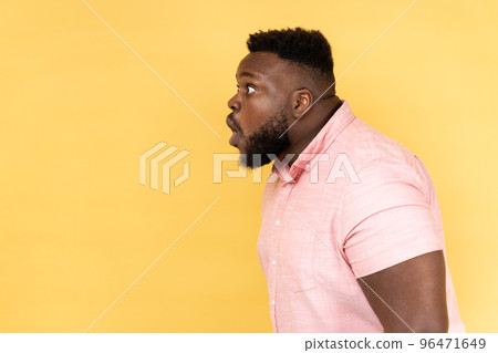 Wow, unbelievable. Side view of man wearing pink shirt has shocked expression, looking at camera with open mouth and amazed big eyes. Indoor studio shot isolated on yellow background. 96471649