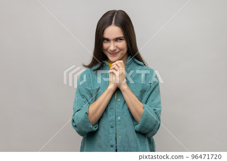 Devious cunning young woman with dark hair clasping hands and smirking mysteriously, scheming cheats, evil prank, wearing casual style jacket. Indoor studio shot isolated on gray background. 96471720