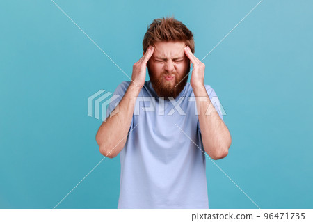 Portrait of unhealthy bearded man massaging temples feeling headache, suffering migraine or high blood pressure, trying to concentrate. Indoor studio shot isolated on blue background. 96471735