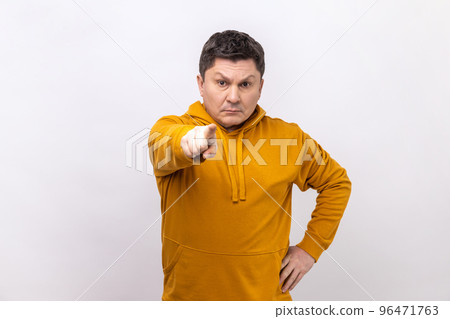 Serious middle aged man pointing finger, indicating direction to camera and looking annoyed, making choice, wearing urban style hoodie. Indoor studio shot isolated on white background. Serious middle aged man pointing finger, indicating direction to camera and looking annoyed, making choice, wearing urban style hoodie. Indoor studio shot isolated on white background. 96471763