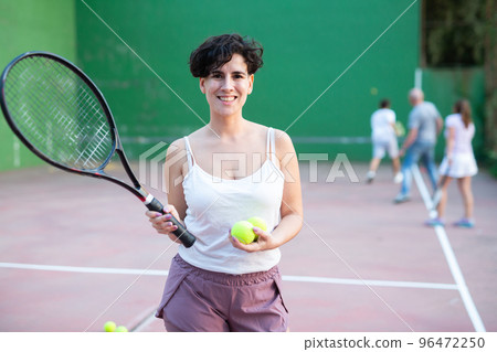 Portrait of latino woman standing on frontenis court, holding racket and ball 96472250