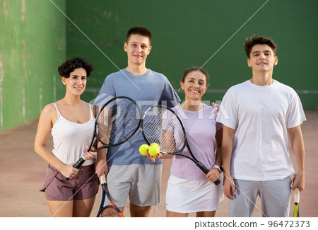 Happy frontenis players with rackets and balls standing in open court 96472373