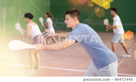 Concentrated young man paleta fronton player hitting ball with racket Concentrated young man paleta fronton player hitting ball with racket 96472449