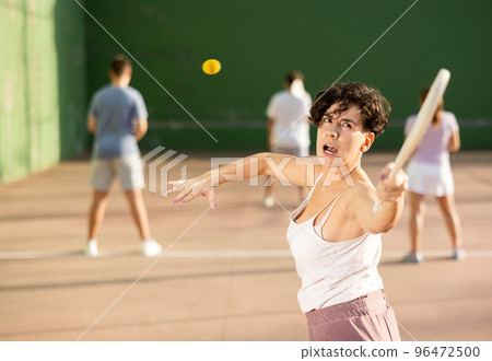 Young Argentinian woman playing pelota at open-air fronton in summer 96472500
