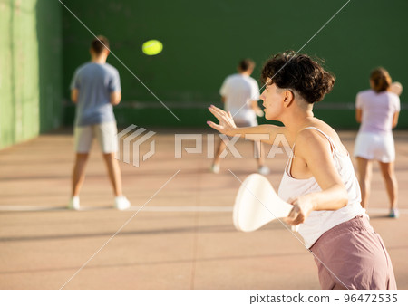 Active womans with enthusiasm playing paleta fronton group on outdoor court Active womans with enthusiasm playing paleta fronton group on outdoor court 96472535