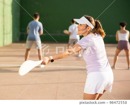 Active womans with enthusiasm playing paleta fronton group on outdoor court 96472558