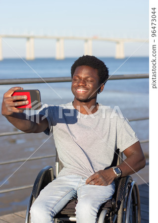 Happy Black guy in wheelchair taking selfie on his mobile phone 96473044